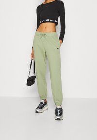 Svart kortärmad topp med långa ärmar, ljusgröna sweatpants med elastisk midja och svarta sneakers. Liten svart väska med axelrem.