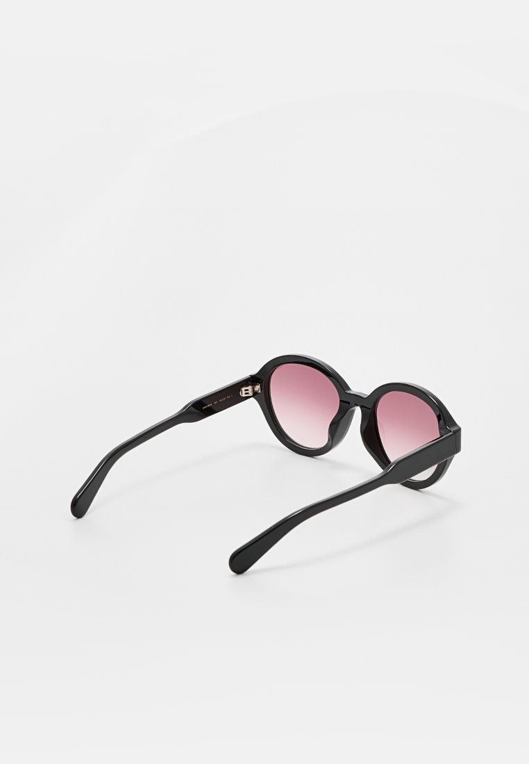 Runde schwarze Sonnenbrillen mit rosa Gläsern, dicken Rahmen und schlanken, gebogenen Bügeln. Auffällige Details am Bügel mit Hardware-Akzenten.