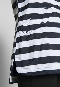 Veste rayée horizontale noire et blanche avec une poche à rabat sécurisée par un bouton-pression noir et le logo "Regatta Great Outdoors" brodé près de l'ourlet.