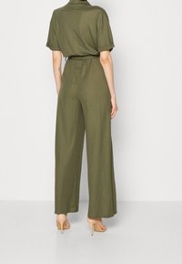 Olivgrön jumpsuit med korta ärmar, vid ben-design, bälte i midjan och mjuk tygkvalitet. Matchas med nude högklackade skor.
