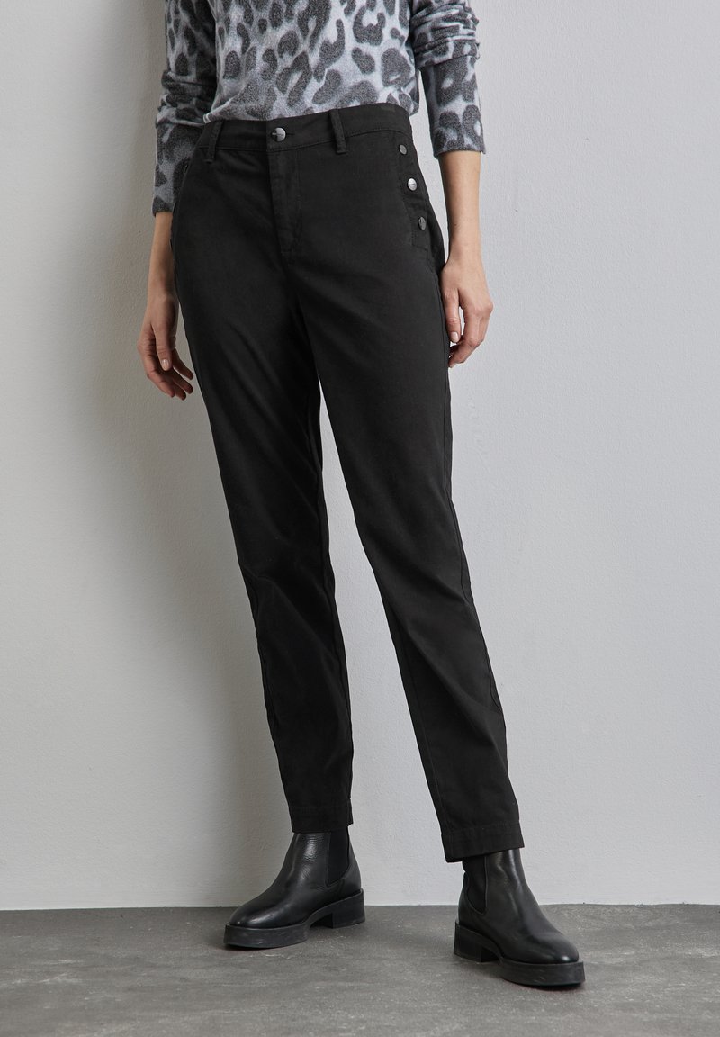 Pantalones negros de tejido suave, con un diseño ajustado, botones laterales y pernera estrecha. Combinados con botas negras de tobillo.