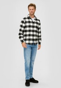 Zwart-witte geblokte flanellen shirt met knopen, gecombineerd met lichtblauwe spijkerbroek en zwarte schoenen, met lange mouwen en een kraag.