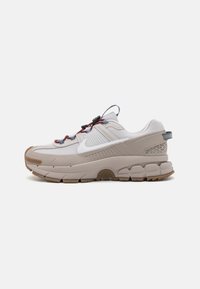 Nike tenisica s svijetlosivim gornjim dijelom i teksturiranim detaljima, te debelim gumenim potplatom. Ima uzorčane vezice i detalj s logom sa strane.