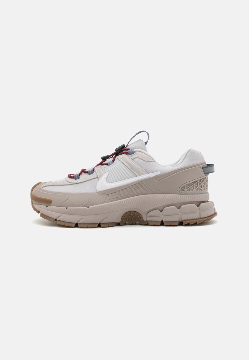 Nike tenisica s svijetlosivim gornjim dijelom i teksturiranim detaljima, te debelim gumenim potplatom. Ima uzorčane vezice i detalj s logom sa strane.