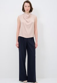 Blusa senza maniche color beige drappeggiata abbinata a pantaloni a gamba larga navy a vita alta. Texture liscia con silhouette casual e rilassata.