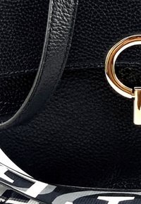 Sac à main en cuir noir avec une finition texturée, du matériel doré et une bandoulière avec logo blanc contrastant. Détail accent circulaire métallique.