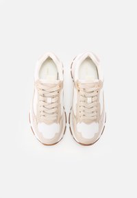 Sneaker mit einem weißen Mesh-Obermaterial, beigen Akzenten und einem strukturierten Design. Besitzt flache Schnürsenkel und eine braune Gummisohle.