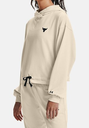 Beżowa bluza z kapturem i pasujące spodnie z czarnym sznurkiem, czarne logo byka na piersi oraz logo Under Armour na rękawie i spodniach.