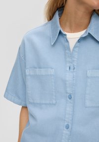 Light blue short-sleeved shirt made of denim, featuring a pointed collar, two chest pockets, and button closure along the front.