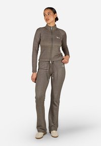 Dviejų dalių apranga su grioveliais, megzta struktūra. Užtrauktuku užsegama striukė ir kelnės yra prispaustos rudos spalvos, turi raištelį ir subtilų logotipo detalę.