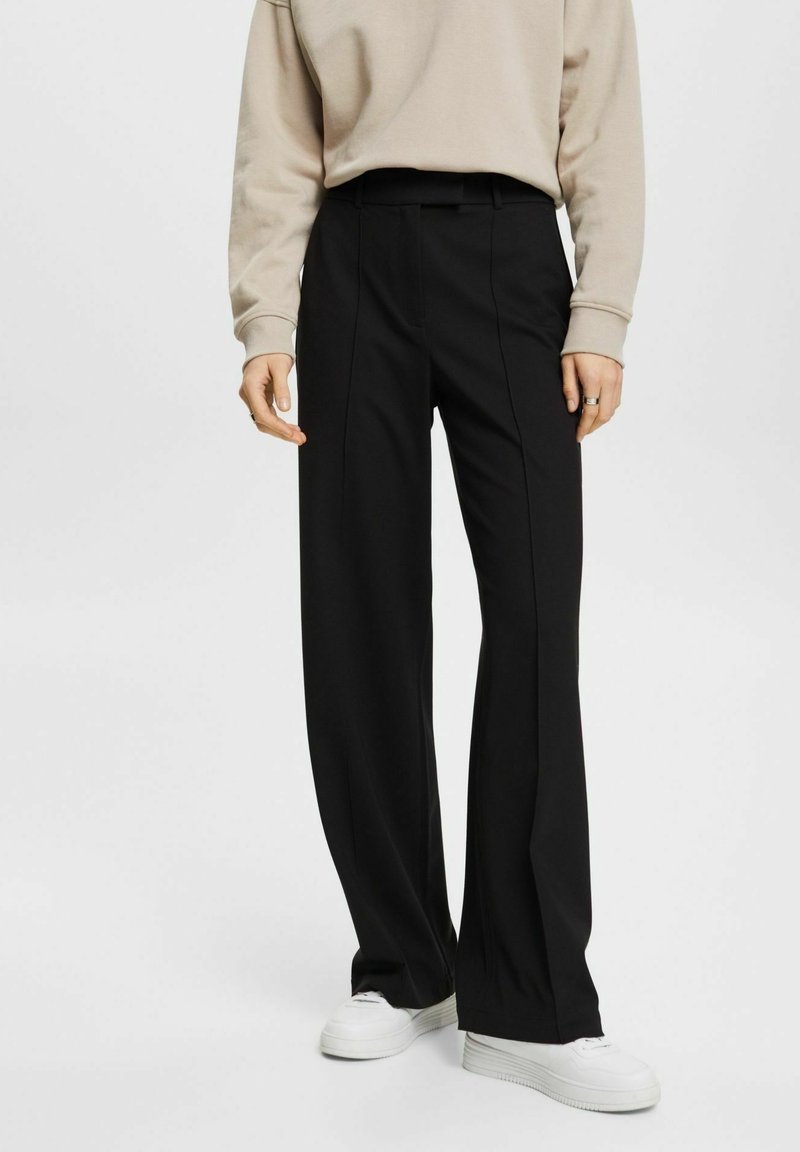 Svarta vida byxor i ett mjukt tyg, med en skräddarsydd design och framfickor. Kombineras med en ljusbeige sweatshirt och vita sneakers.