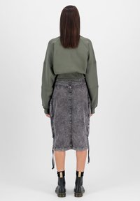 Zöld, cropped fazonú pulóver hosszú ujjakkal, szürke farmer szoknyával párosítva, amely oldalzsebekkel és húzózsinóros részletekkel rendelkezik. Fekete bokacsizmák.