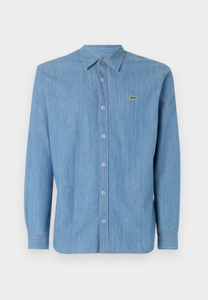 Helles blaues Jeanshemd mit einem Kentkragen, langen Ärmeln und einem kleinen gestickten Logo auf der linken Brust. Mit Knopfverschluss auf der Vorderseite.