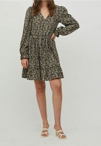 Svart blommig klänning med långa puffärmar, V-ringning och låttrappad kjol. Bärs med krämfärgade sandaler med remmar.