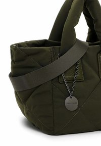 Dunkelgrüne gesteppte Stoffhandtasche mit gepolsterten Griffen, einem breiten Schultergurt und einem runden Metallmarkenanhänger an einer Kette.