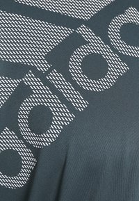 Närbild av mörk tyg med stora vita bokstäver som visar en del av ordet "SPORT" i ett diagonalt mönster.