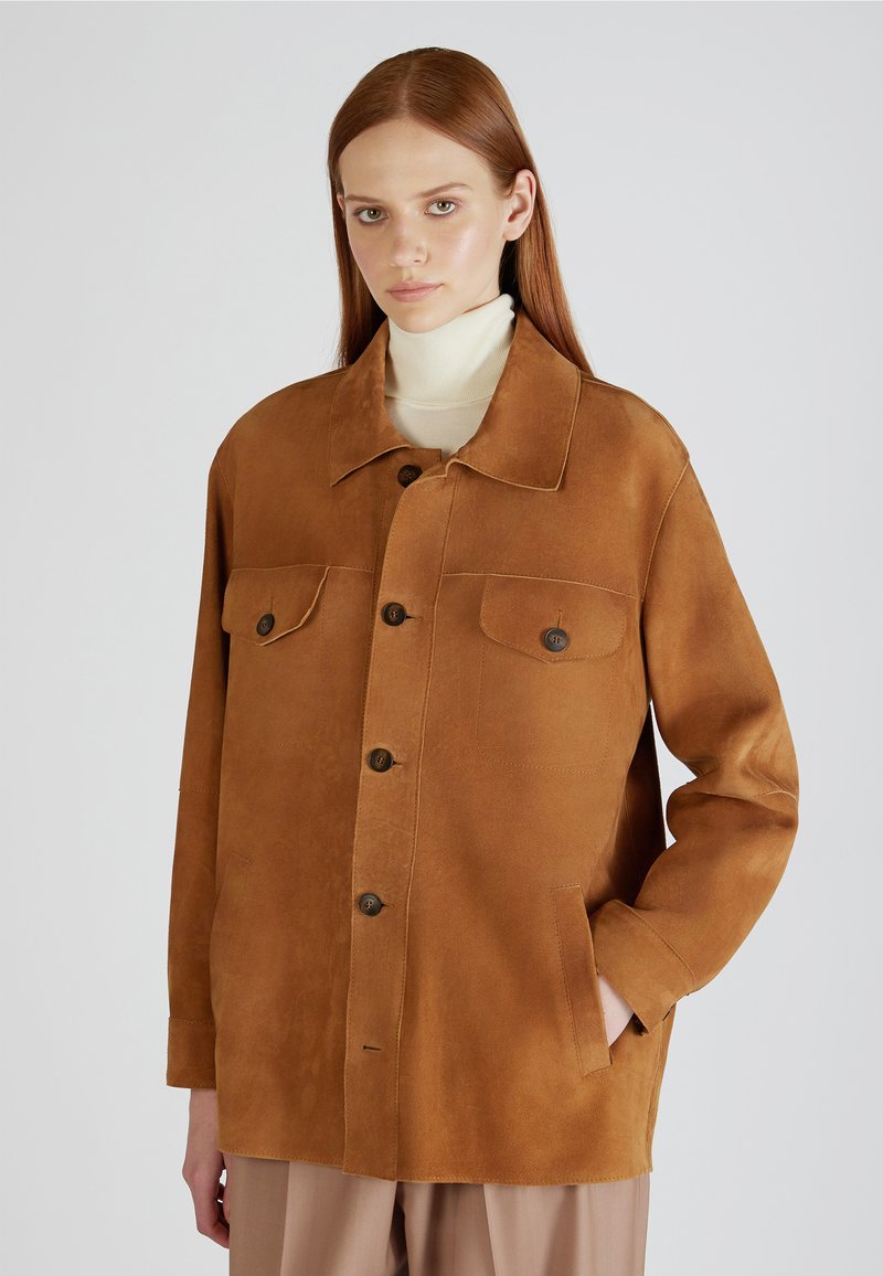 Veste en daim marron avec un col, fermeture à boutons, deux poches avant et manches longues, présentant une texture lisse et une coupe décontractée.