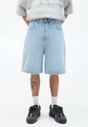 Light blue denim shorts with a relaxed fit, knee-length, and frayed hem. Paired with black sneakers and white socks.