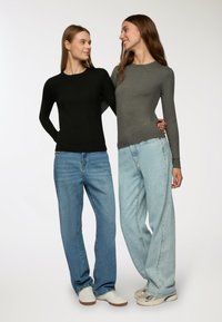 Dwie modelki noszą dopasowane topy z długim rękawem; jedna w czarnym, a druga w szarym. Obie mają na sobie luźne, jasnoniebieskie dżinsy i białe sneakersy.