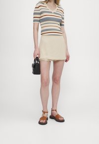 Kortärmad, randig stickad topp i beige, orange och marinblå; beige minikjol; svart handväska; bruna sandaler med kraftig sula.