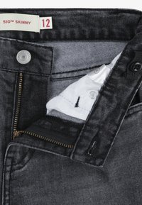 Jeans de mezclilla negra con corte ajustado, que cuentan con un cierre de cremallera, botón y un bolsillo interior. La etiqueta indica talla 12, estilo 510™ Skinny.