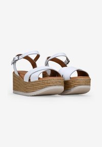 Sandalias de cuña blancas con detalle de yute trenzado, correa ajustable en el tobillo, diseño de punta abierta y una textura suave similar al cuero.