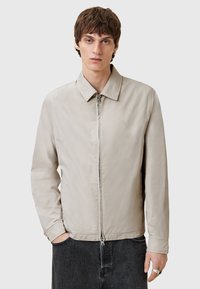 Beige lichtgewicht jack met een kraag, ritssluiting aan de voorkant en elastische manchetten. Heeft een subtiele logo op de borst en een gladde textuur.