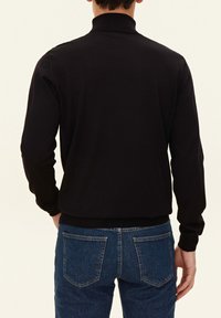 Schwarzer Rollkragenpullover mit geripptem Kragen und Bündchen, kombiniert mit blauen Denim-Jeans im klassischen Fünf-Pocket-Design.