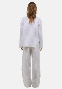 Ensemble de pyjama rayé en blanc et gris clair, comprenant un haut ample à manches longues et un pantalon large assorti avec un accent au niveau de l'ourlet.