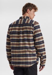 Camicia in flanella con motivo a quadri nei toni beige, navy e marrone. Tessuto morbido, polsini con bottoni e colletto con design a yoke sul retro.