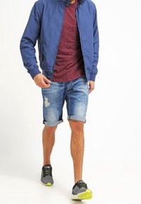 Modrá bomber bunda, vínová košile, roztrhané džíny šortky a šedé tenisky se žlutými akcenty. Neformální oblečení na teplé počasí.