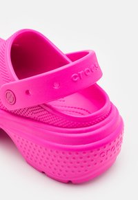 Sandale Crocs rose vif avec un design texturé, une large sangle et un dessus perforé. Matériau en caoutchouc doux avec une semelle rembourrée.