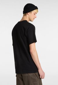 Sort bomulds-t-shirt med korte ærmer, rund halsudskæring og afslappet pasform, parret med mørke, strukturerede cargo-bukser. Sort strikket beanie båret.