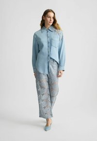 Camicia di jeans azzurri con design a bottoni, abbinata a pantaloni azzurri con paillettes a motivo merletto. Il modello indossa décolleté blu a punta.