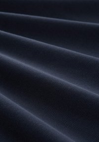 Temno modra tkanina z teksturiranim, pletenim vzorcem, ki prikazuje drobne rebraste vzorce in gladke, tekoče drape po površini.