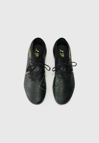 Black soccer shoes with a textured upper, featuring green accents and laces, a low profile, and a streamlined shape.