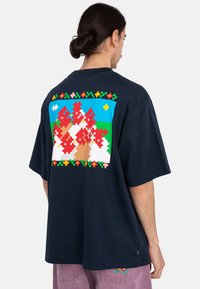 Camiseta de algodón azul marino con un gran diseño de pieza de rompecabezas colorida en la parte posterior, con flores y una escena paisaje. Corte holgado, mangas cortas.