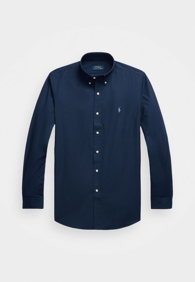 Ναυτικό μπλε πουκάμισο με μακριά μανίκια και κουμπιά, φτιαγμένο από βαμβάκι, με κλασικό γιακά, διακοσμημένο με ένα μικρό κεντημένο λογότυπο στο στήθος και λεπτομέρειες με κουμπιά.