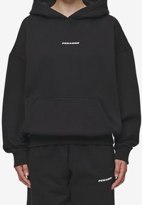 Sudadera con capucha negra hecha de mezcla de algodón, que cuenta con un bolsillo en la parte frontal y el logo "PEGADOR" en blanco en el pecho, junto con pantalones de chándal negros a juego.