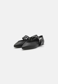 Chaussures noires plates en cuir lisse, avec un bout pointu et une sangle de cheville ornée de clous en métal ronds et d'une boucle argentée.