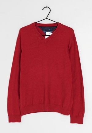 Suéter rojo de manga larga con cuello en V colgado en una percha negra contra un fondo blanco, con etiqueta de marca y etiqueta de precio visibles dentro del cuello.