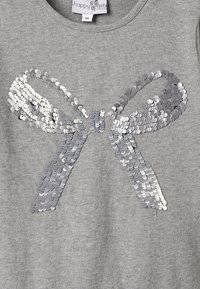 Šedá mikina s velkou dekorativní mašlí vyrobenou z stříbrných flitrů, která vykazuje různé odstíny šedé a má hladkou texturu látky.