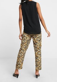 Černý top bez rukávů spárovaný s žluto-černými kalhotami s tygřím vzorem, které mají volný střih a hladký materiál. Celkový vzhled doplňují černé lodičky na vysokém podpatku.