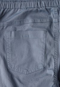 Ljusblå vävd tyg med resårmidja. Har en rektangulär bakficka, överstygnade detaljer och en slät yta.