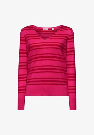Różowy sweter w paski z dekoltem w serek i długimi rękawami, zestawiony z wysokim stanem niebieskich dżinsów. Widoczna mała biała torebka i srebrne pierścionki.