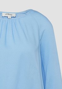 Hellblaue Bluse mit langen Ärmeln, rundem Ausschnitt und kleinen Falten unter dem Kragen, mit s.Oliver Markenetikett am Krageninneren.
