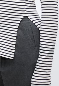 Fehér és tengerészkék csíkos hosszú ujjú felső, szürke, enyhén fényes nadrággal párosítva. Jellegzetes oldalsó slicc a felsőn.