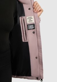 Polstret jakke indvendig i lys pink med sort foer. Har mærker på venstre side og trykknapslukninger. Glat tekstur og quiltet mønster.