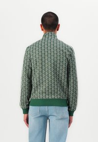 Zelená bomber bunda so vzorom, s vysokým golierom, rebrovanými manžetami a lemom, s geometrickým dizajnom a kontrastnými bočnými pruhmi.
