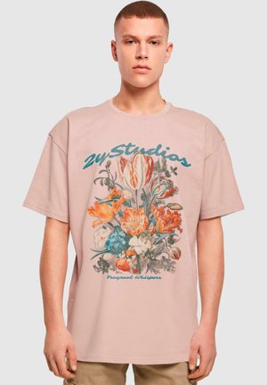 Camiseta de algodón rosa claro con un ajuste holgado, que presenta un diseño gráfico floral en naranja y azul, y el texto "24 Studios" en la parte superior.